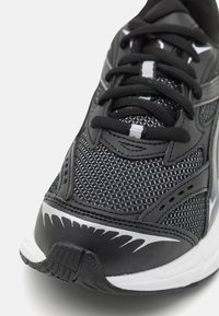 Czarne buty sportowe z siateczkową górą, zaokrąglonym noskiem, jednolitymi sznurowadłami, białymi akcentami i teksturowaną podeszwą. Projekt zawiera sportowe detale.