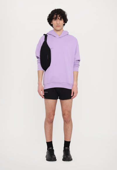Fioletowy hoodie, czarna torba na ramię, czarne szorty i czarne sneakersy. Teksturowany materiał z prążkowanymi mankietami i nadrukowanymi detalami.