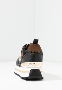 Svart och brun sneaker med en texturerad mockaöverdel, guldaccent på hälen och en tjock vit och svart sula med gummitread.