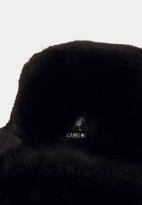Sombrero de piel negra con textura suave, parte superior redondeada y un sutil detalle de logo. El diseño cuenta con un material esponjoso y liso.