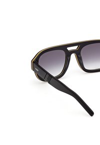 Mustat aurinkolasit kiiltävällä pinnalla, joissa on rohkea muotoilu, liukuväriset linssit ja hoikka kehys, jota korostaa kultainen viiva reunoilla.