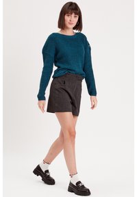 Pull en tricot teal avec une coupe ample, short gris ajusté et mocassins noirs. Chaussettes blanches avec des bords volants et un motif de petits coeurs.