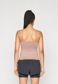 Top débardeur marron ajusté avec fines bretelles, texture lisse et détail logo. Associé à un short de sport noir avec un design superposé.