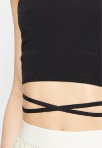 Top cropped preto com um design justo, apresentando alças finas cruzadas na cintura e uma textura suave e elástica.