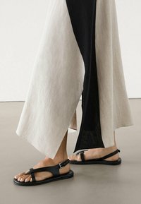 Zwarte platte sandalen met een minimalistisch ontwerp. Voorzien van een gespclosure en meerdere banden. Draag ze met een vloeiende tweekleurige jurk.