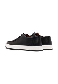 Scarpe in pelle nera con finitura testurizzata, suola in gomma bianca e cuciture a contrasto. Presentano lacci e un design a profilo basso.