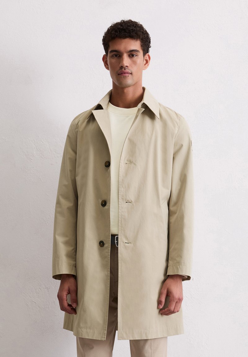 Lichtbeige trenchcoat met een notch-kraag, knopenfront en een losse pasvorm. Voorzien van lange mouwen en een gladde, lichte stof.