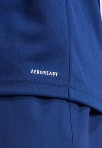 Navyblauwe sportstof met het "AEROREADY" logo in het wit. Textuur oppervlakte met gladde gedeelten, die de contrasterende ontwerpelementen benadrukken.