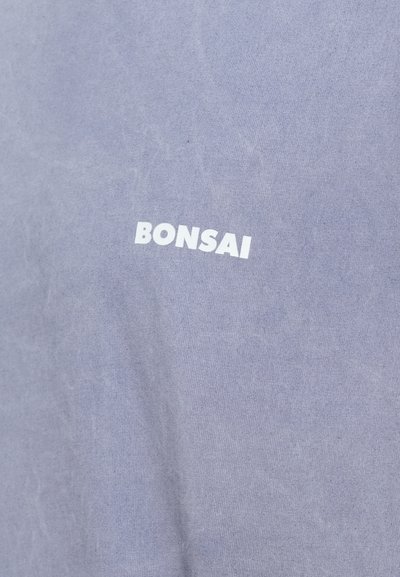 Tricou din bumbac gri cu o textură moale, având cuvântul "BONSAI" scris cu litere albe, îndrăznețe, pe față. Design simplu și minimalist.