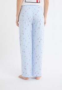 Pantalon de pyjama bleu clair à coupe ample, présentant un imprimé ludique et dispersé de petites figures colorées sur tout le tissu.
