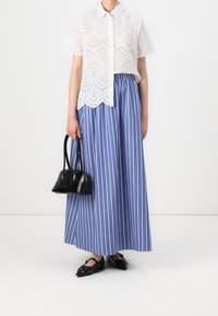 White eyelet blouse with short sleeves, paired with a blue and white striped maxi skirt. Holding a small black handbag, wearing black flats.