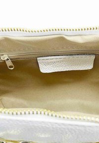 Hvid læder håndtaske indvendig med beige foring, udstyret med en lynlås-lomme og et lille mærke syet indeni. Gullige lynlåsbeslag synlige.