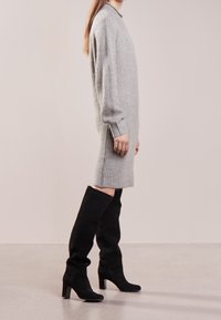 Robe en tricot gris clair avec une texture côtelée et des manches longues, associée à des bottes noires en daim montantes jusqu'au genou avec un talon carré.