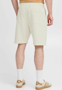 Shorts beige clair avec une taille élastique, dotés d'une poche arrière et d'une texture lisse, associés à des chaussettes blanches et des chaussures avec des accents marron.