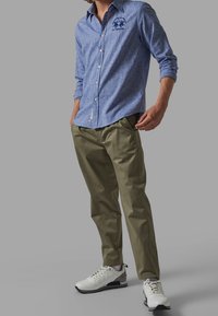 Ljusblå knäppt skjorta med palmer broderade, kombinerad med olivgröna byxor och vita sneakers med grå detaljer. Avslappnad passform och design.