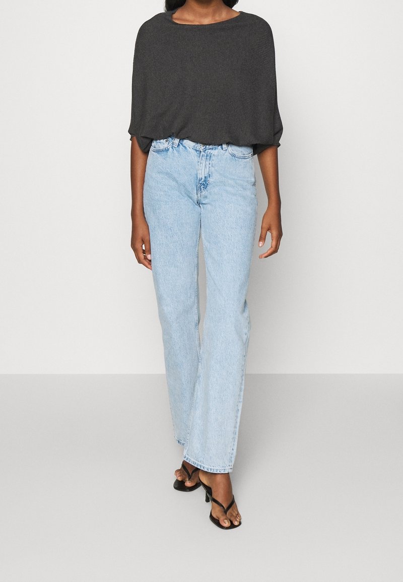 Graues, locker sitzendes Oberteil mit weiter Ausschnitt und kurzen Ärmeln, kombiniert mit hellblauen, hoch taillierten, geraden Jeans und schwarzen Sandalen.