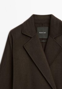 Hnědý vlněný kabát s klopovým límcem, vystavený od oblasti ramene. Uvnitř má štítek s názvem "Massimo Dutti". Měkká textura.