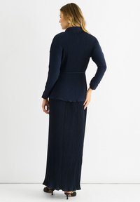 Navy pleated dress set with a long-sleeve top and a flowing skirt. The fabric has a textured finish with a subtle sheen.