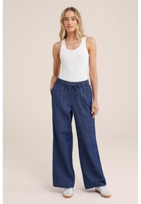 Mørkeblå vide bukser med elastisk talje og snor, parret med en hvid tanktop og hvide sneakers. Glat tekstur.
