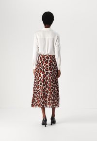 Camicia bianca a maniche lunghe e una gonna maxi fluida con stampa leopardata in tonalità di arancione e marrone. L'outfit è completato da scarpe nere con tacco.