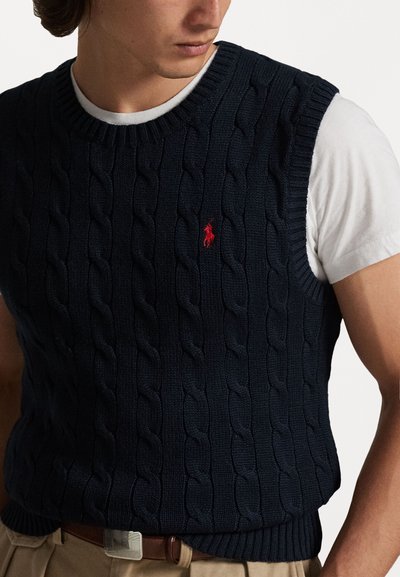 Tamsiai mėlynas megztas liemenė, pagaminta iš tekstūruotos medžiagos, su apvaliu iškirpimu ir mažu raudonu logotipu ant krūtinės.