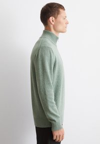 Grüner Strickpullover mit Rollkragen, gerippten Bündchen und Saum, der ein strukturiertes Muster aufweist. Entworfen für eine figurnahe Silhouette.