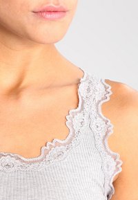 Grå ribbet tanktop med blondekant langs halsen, med scalloped kant og delikate blomster mønstre. Myk tekstur.