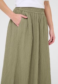 Khaki rok van een gestructureerde, gekreukte stof met een elastische tailleband. Heeft zijzakken en een vloeiende snit.
