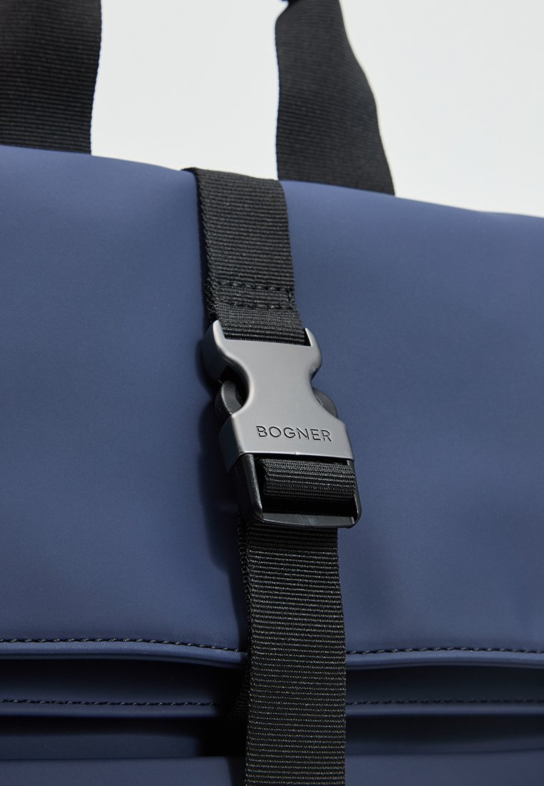 Niebieska torba z czarnym regulowanym paskiem i srebrną klamrą, na której wygrawerowana jest nazwa marki "BOGNER".