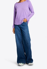 Lila Langarmshirt mit Rundhalsausschnitt, kombiniert mit lockeren blauen Jeans und hellen Sneakers mit grünen Akzenten.
