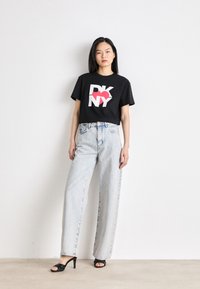 Svart kortermet t-skjorte med hvit og rød "DKNY" logo. Kombinert med høyhåndtaks lyseblå vide jeanstype og svarte hælede sandaler.