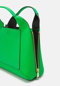 Zelená kožená taška s texturovaným povrchem, černými akcenty, dvojitými uchy a detailním zlatým zipem po straně. Obsahuje obdélníkovou přední kapsu.