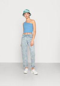 Top cropped azul claro com uma alça, combinado com jeans de lavagem clara com design em patchwork e ténis brancos. Chapéu de balde verde.