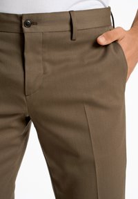 I pantaloni eleganti marroni presentano una texture liscia, una chiusura con bottone e tasche laterali. La vestibilità è tailored, con un design pulito e strutturato.