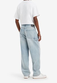 Jeans de color azul claro, de corte holgado y cintura alta, con costuras visibles y dos bolsillos traseros. Llevados con una camiseta blanca corta y zapatillas blancas.