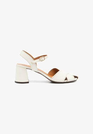 Sandalo aperto in pelle bianca con tacco a blocco e cinturino alla caviglia regolabile con fibbia, mostrato di lato su uno sfondo bianco.