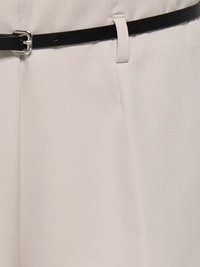 Beżowe spodnie materiałowe z czarnym teksturowanym paskiem. Pasek ma srebrną klamrę i jest przewleczony przez szlufki w pasie.