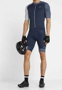 Herrcykeloutfit med en marinblå tröja med geometriska mönstrade ärmar och matchande shorts. Svart hjälm och cykelskor ingår.