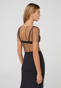 Top in rete nero con maniche corte, decorato con perline, abbinato a una gonna nera uniforme. Il design scoperto mette in evidenza la schiena aperta e le spalline.