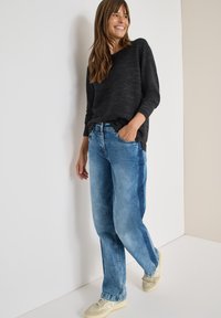 Zwart textuur langmouwtop gecombineerd met lichtblauwe, loszittende jeans. Zichtbare details zijn onder andere zakken en een ontspannen silhouet.