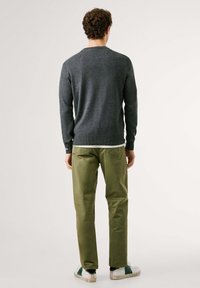 Suéter de punto gris con mangas largas, cuello redondo y dobladillo acanalado; combinado con pantalones verde oliva y zapatillas blancas con acentos verdes.