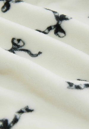 Fleece fabric featuring a cream background with black bow patterns, soft texture, and subtle sheen, displaying gentle folds and layers.