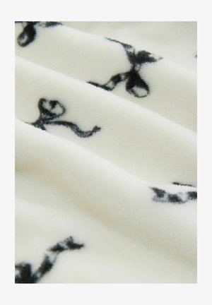 Fleece-tyg med en krämfärgad bakgrund och svarta snöringsmönster, mjuk textur och subtil lyster, som visar mjuka veck och lager.