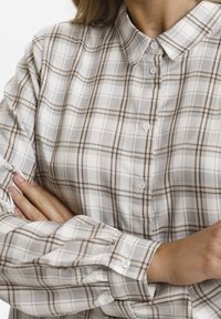 Chemise à carreaux aux tons crème et marron ; dotée d'un col classique, de poignets à deux boutons et d'une texture tissée douce.