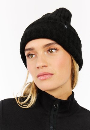 Black knitted beanie with ribbed texture, featuring an upright peak. Worn with a black zip-up fleece jacket.