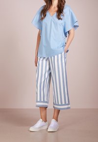 Top azzurro chiaro con scollo a V e maniche corte svasate, abbinato a culotte larghe a righe blu e bianche, e sneaker bianche.
