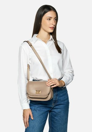 Borsa a tracolla in faux leather beige con chiusura in tonazione oro; presenta una forma strutturata e una tasca piatta sulla parte anteriore. Indossata con jeans blu e camicia bianca.