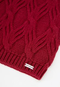 Rode gebreide sjaal met een gestructureerd kabelpatroon en een geribbelde rand. Label met de tekst "Wittchen" nabij de onderkant.