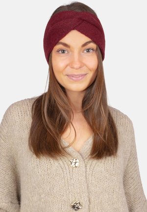 Bordeauxrotes, gestricktes Stirnband mit verdrehtem Frontdesign, weicher Textur, abgerundeten Kanten und gemütlichem Aussehen, getragen mit einer beigen Strickjacke.