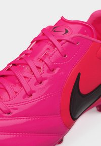 Φωτεινό ροζ ποδοσφαιρικό παπούτσι Nike με μαύρο λογότυπο Swoosh και ροζ κορδόνια, εμφανίζεται σε κοντινή λήψη από ψηλά.